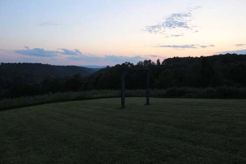 Sunset over rolling hills with two standing stones in a grassy field, creating a serene landscape.