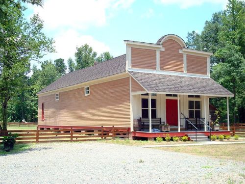 A charming wooden building with a sloped roof, red doors, and surrounded by trees and gravel, resembling a small town structure.