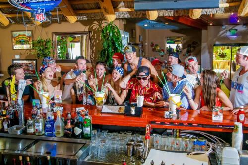 A lively group of young people at a bar, enjoying drinks and having fun, with colorful decorations in the background.