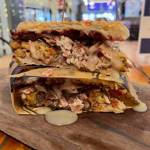 A stacked sandwich with shredded meat, sauce, and crispy bread, served on a wooden board in a cozy setting.