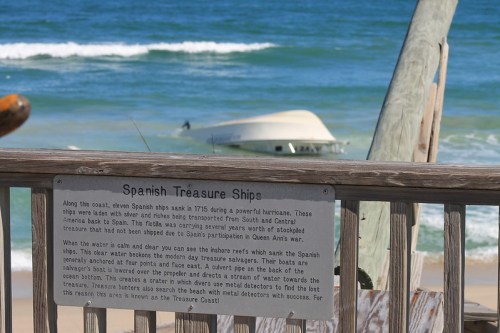 Sign about Spanish treasure ships wrecked in 1715, with a view of the ocean and a sunken boat in the background.