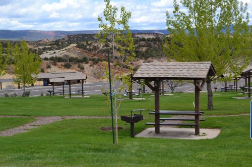 A grassy park area with picnic tables, trees, and a scenic view of hills and clouds in the background.