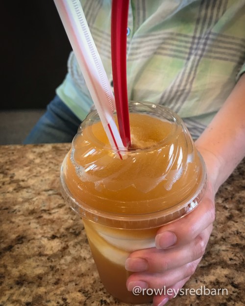 A person holds a large drink with a swirl of colors, topped with two straws, on a countertop.