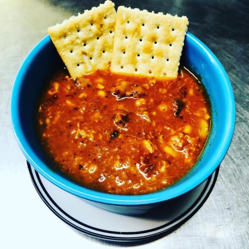 A blue bowl filled with chili, topped with two saltine crackers, on a black and white plate.