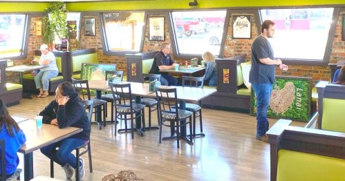 A casual dining area with green accents, featuring several tables and patrons enjoying their meals.