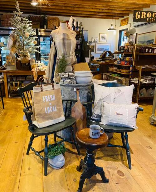 A cozy shop display featuring chairs, pillows, a tote bag, and rustic decor on wooden floors.