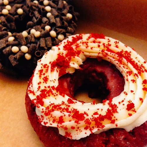 Two donuts: one with red velvet frosting and sprinkles, the other topped with chocolate and white candy pearls.