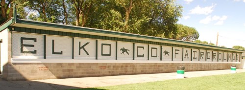 Sign on a building at Elko County Fairgrounds, featuring large letters spelling "ELKO CO. FAIRGROUNDS" against a blue sky.