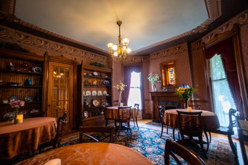 Elegant vintage dining room with ornate decor, wooden furniture, and a stained glass window, featuring tables and floral arrangements.