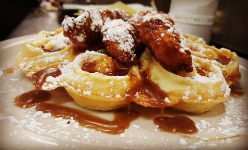 A plate of waffles topped with powdered sugar and fried pieces, drizzled with caramel sauce.