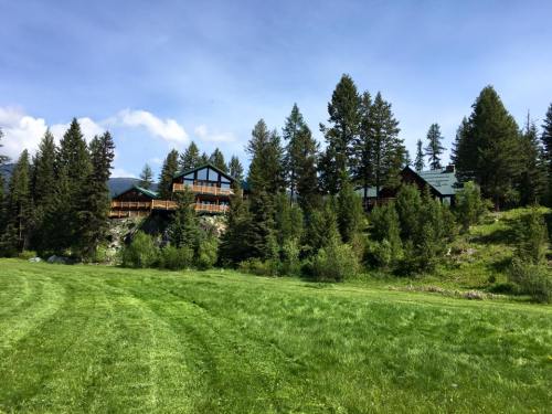 A scenic view of two wooden cabins nestled among tall trees, set against a backdrop of blue sky and green grass.