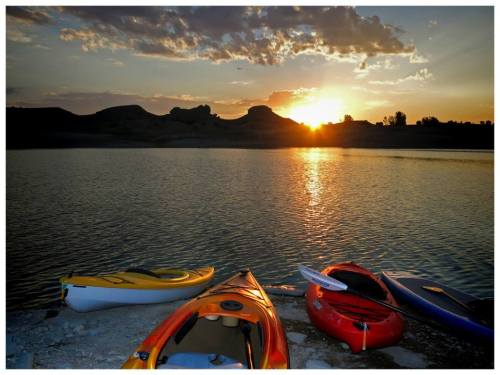 Kayaks on the shore at sunset, with a calm lake and silhouetted hills in the background.
