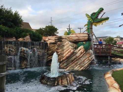 A whimsical mini-golf scene featuring a dragon statue, waterfalls, and a fountain amidst lush greenery.
