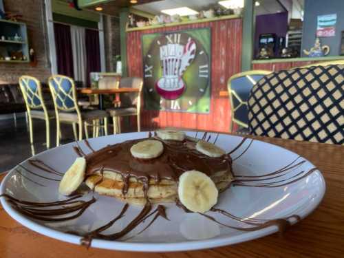 A plate of pancakes topped with banana slices and drizzled with chocolate, set in a cozy café.