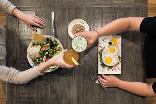 Two people clink glasses over a table with salads, eggs, and desserts, enjoying a meal together.
