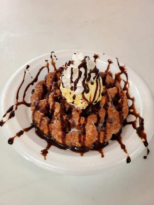 A delicious waffle topped with ice cream, whipped cream, and drizzled with chocolate sauce on a white plate.