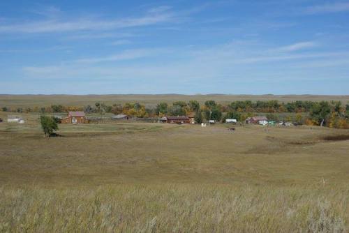 A wide view of a rural landscape featuring a small cluster of buildings surrounded by open fields and distant hills.