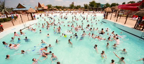 A crowded water park pool filled with people enjoying the water on a sunny day.