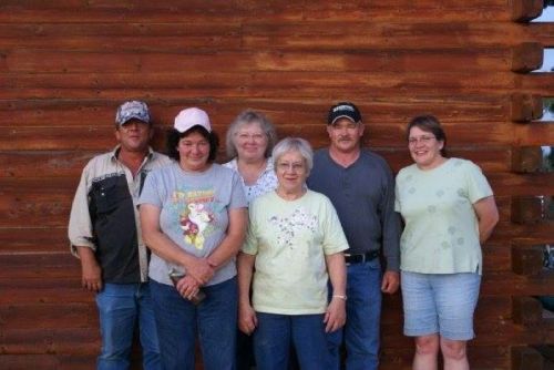 A group of six people standing together in front of a wooden wall, smiling and posing for the photo.