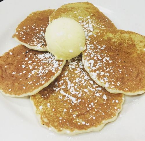A plate of fluffy pancakes topped with a scoop of butter and dusted with powdered sugar.