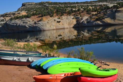 Colorful kayaks and canoes lined up on a sandy shore, reflecting in calm water surrounded by rocky hills.