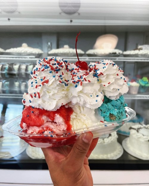 A hand holding a colorful ice cream sundae topped with whipped cream, sprinkles, and a cherry.