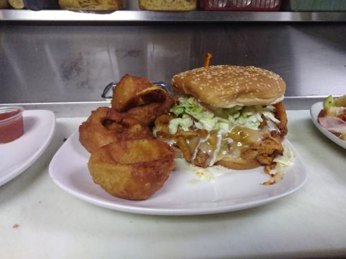 A sesame seed bun burger with lettuce and sauce, served with crispy onion rings on a white plate.
