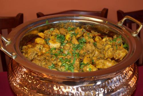 A large silver serving dish filled with spiced chicken, garnished with fresh herbs, on a table.