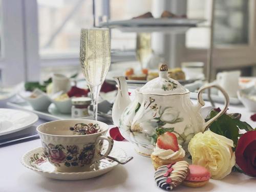 A beautifully set table with a teapot, teacup, champagne flute, and assorted pastries, surrounded by rose petals.