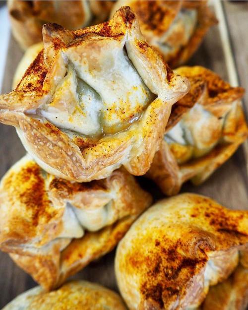 A close-up of golden-brown pastries with a flaky crust, topped with a sprinkle of paprika, arranged on a wooden surface.