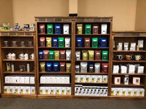 A wooden shelf displaying various tea and coffee products in colorful packaging, with mugs and teapots below.