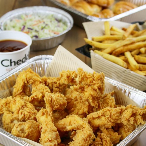 A spread of crispy fried chicken, coleslaw, and dipping sauce in takeout containers on a wooden table.