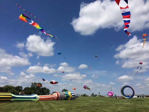A vibrant sky filled with colorful kites and banners flying over a green field under fluffy white clouds.