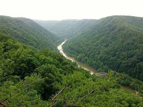 A scenic view of a winding river surrounded by lush green mountains under a cloudy sky.