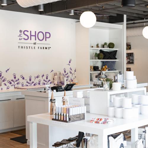 Bright, modern shop interior with white walls, plants, and products displayed on shelves and tables.