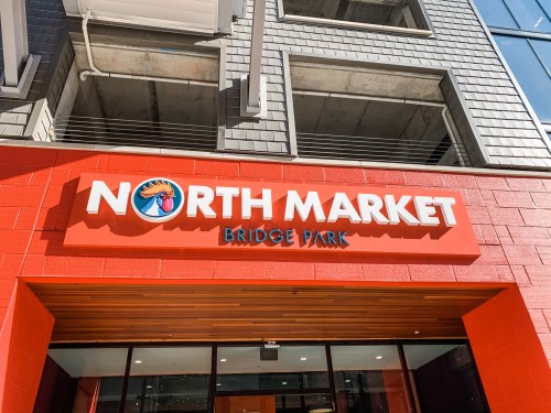 Sign for North Market at Bridge Park, featuring bold red letters and a logo, set against a modern building facade.
