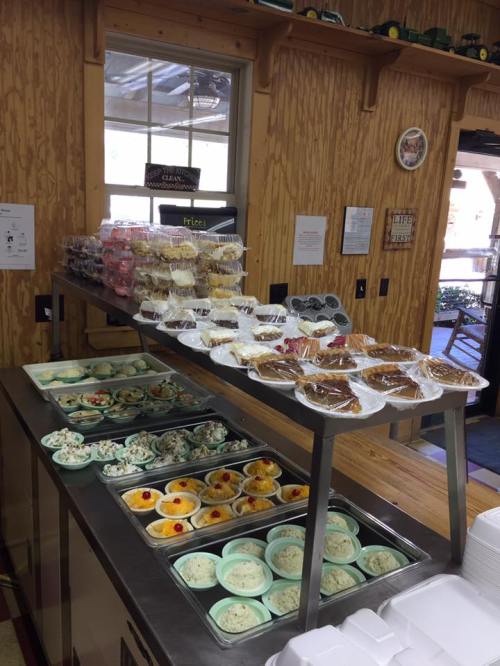 A dessert display featuring various cakes, pastries, and ice cream in cups on a wooden counter.