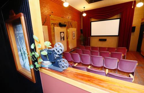 A vintage movie projector sits beside a small, empty theater with red seats and a large screen at the front.