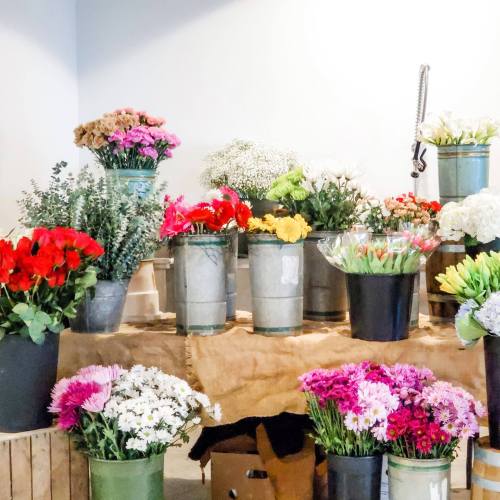 A vibrant flower shop display with various colorful bouquets in metal buckets and pots on a wooden table.