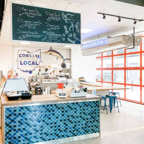 Interior of a seafood restaurant with a chalkboard menu, blue tile accents, and a bright red window wall.