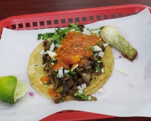 A taco filled with meat, onions, and salsa, served with a lime wedge and grilled onion on a red tray.