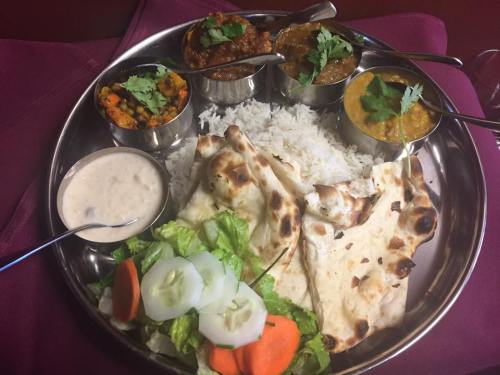 A silver platter with rice, naan, and three bowls of colorful curries, garnished with cilantro, alongside a salad.