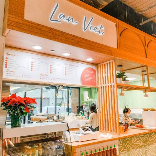 A cozy restaurant interior with a wooden counter, "Lan Viet" sign, and staff preparing food in a bright, inviting space.
