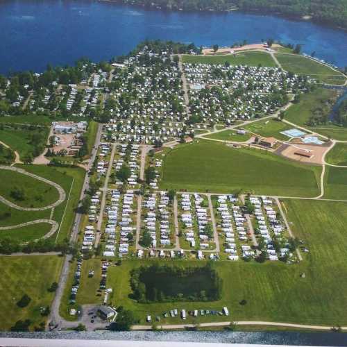 Aerial view of a large campground with numerous RVs, green fields, and a nearby lake.