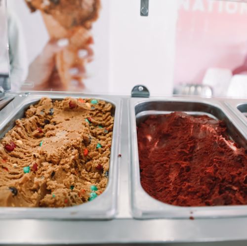 Two tubs of ice cream: one with colorful mix-ins and the other a rich red flavor, displayed in a freezer.