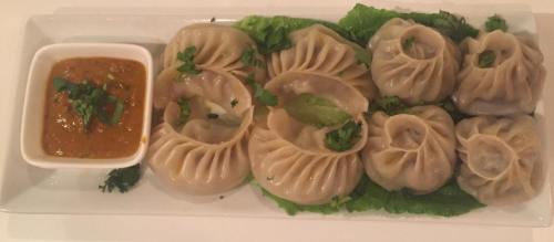A plate of steamed dumplings arranged on lettuce, served with a small bowl of dipping sauce and garnished with herbs.
