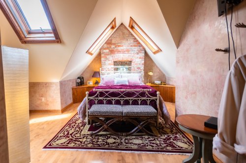 Cozy attic bedroom with sloped ceilings, a brick accent wall, a bed with purple bedding, and a decorative bench.