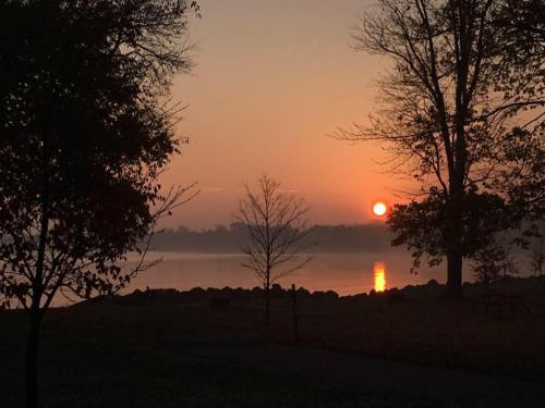 A serene sunrise over a calm lake, with silhouettes of trees and soft orange hues reflecting on the water.