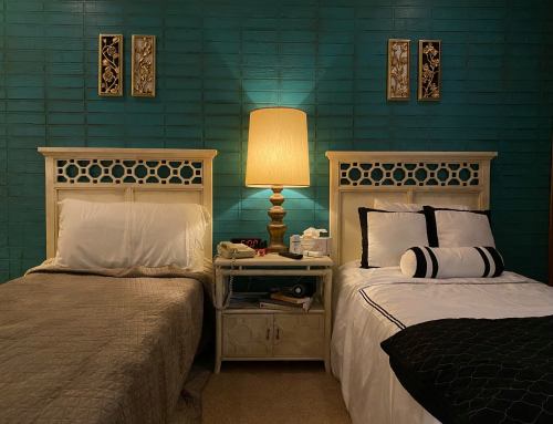 Two twin beds with decorative headboards, a lamp, and nightstands against a teal wall. Cozy and inviting atmosphere.