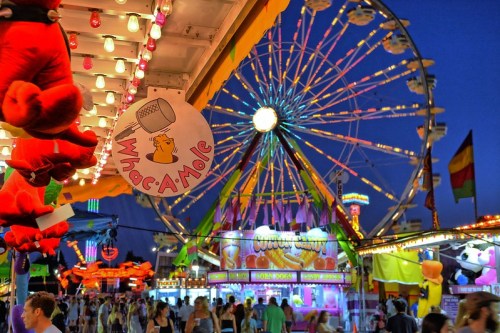 A vibrant carnival scene at night, featuring a Ferris wheel, game booths, and colorful lights.